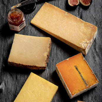 american cheddar flight - four different kinds of cheddar cheese on a cheese board with honey and figs